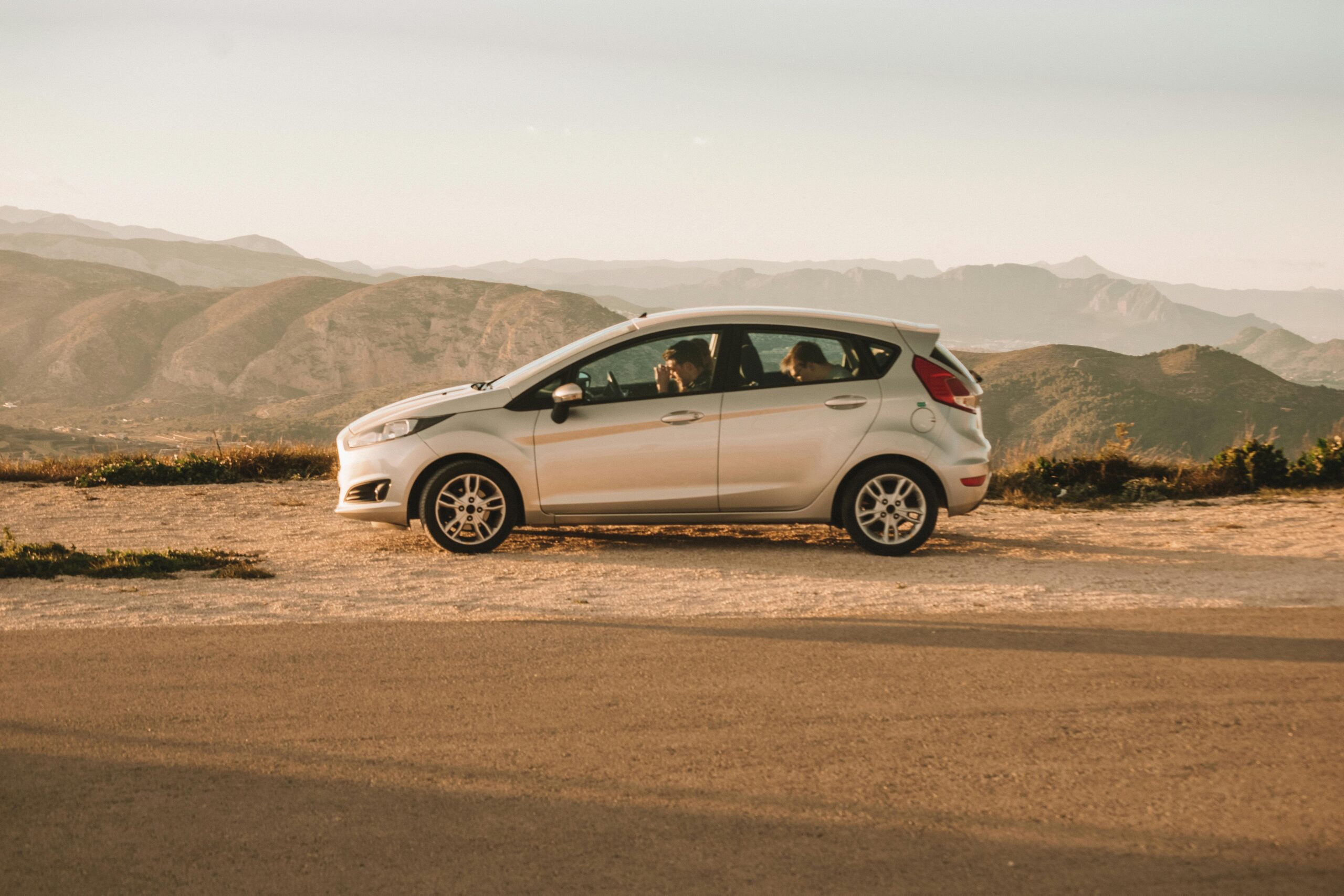 A parked car beside a road with stunning mountainous backdrop in Spain, capturing a serene and picturesque road trip moment.
